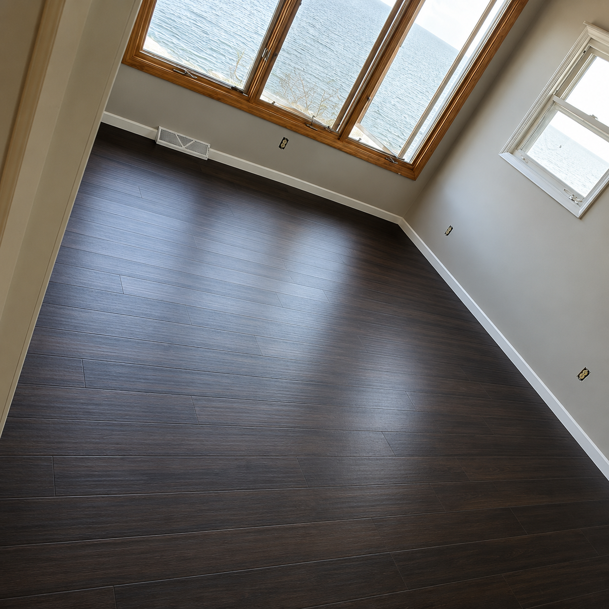Empty room with dark wood floors, white walls, and large windows letting in daylight