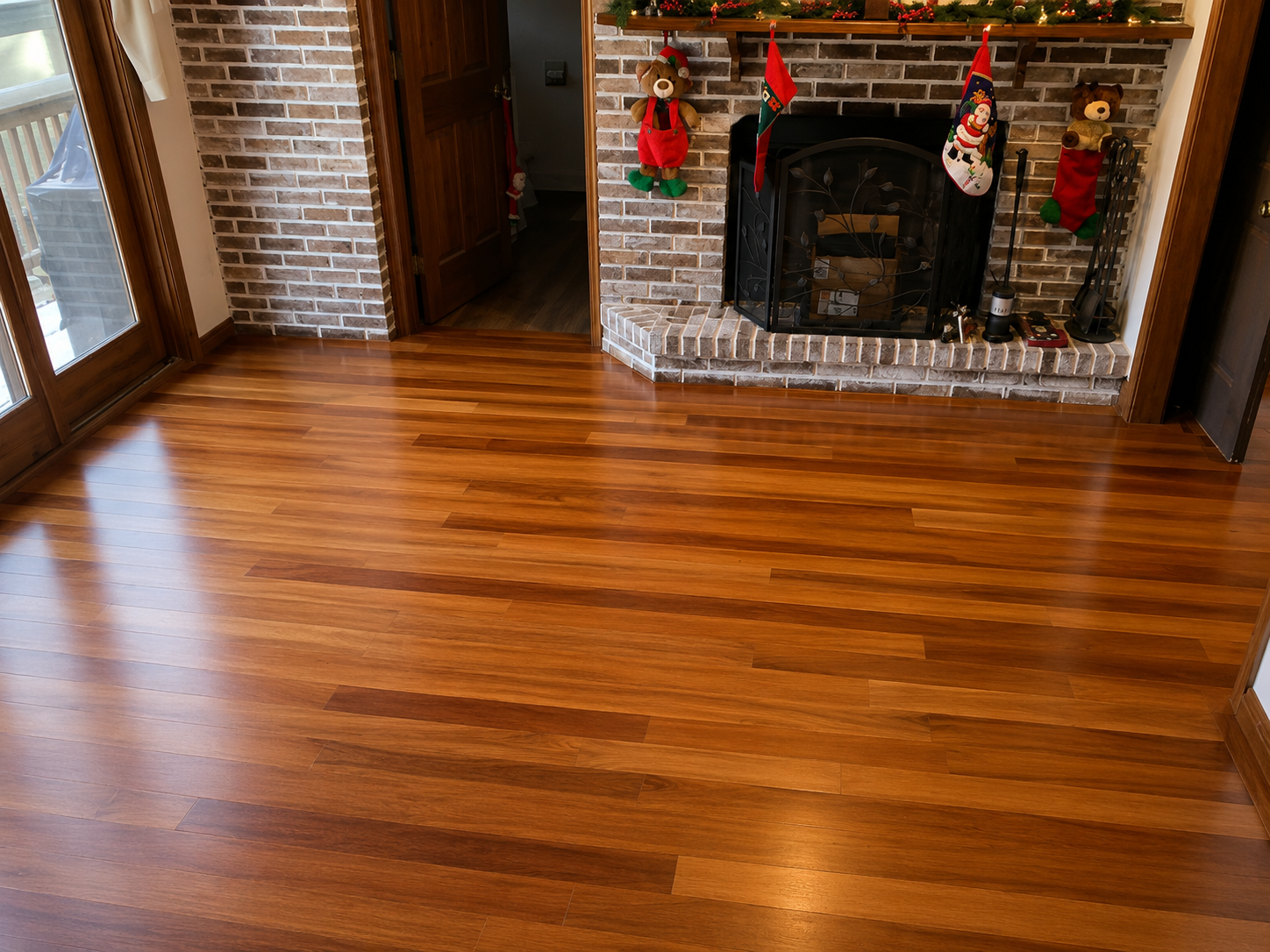 Empty living room with polished hardwood floor and brick fireplace decorated with Christmas stockings.