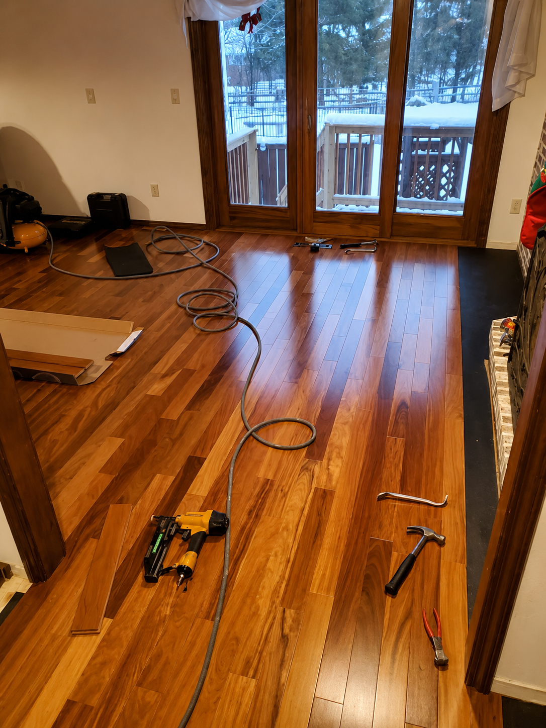 Wooden living room floor with tools and cords during repairs, snow visible through glass doors.