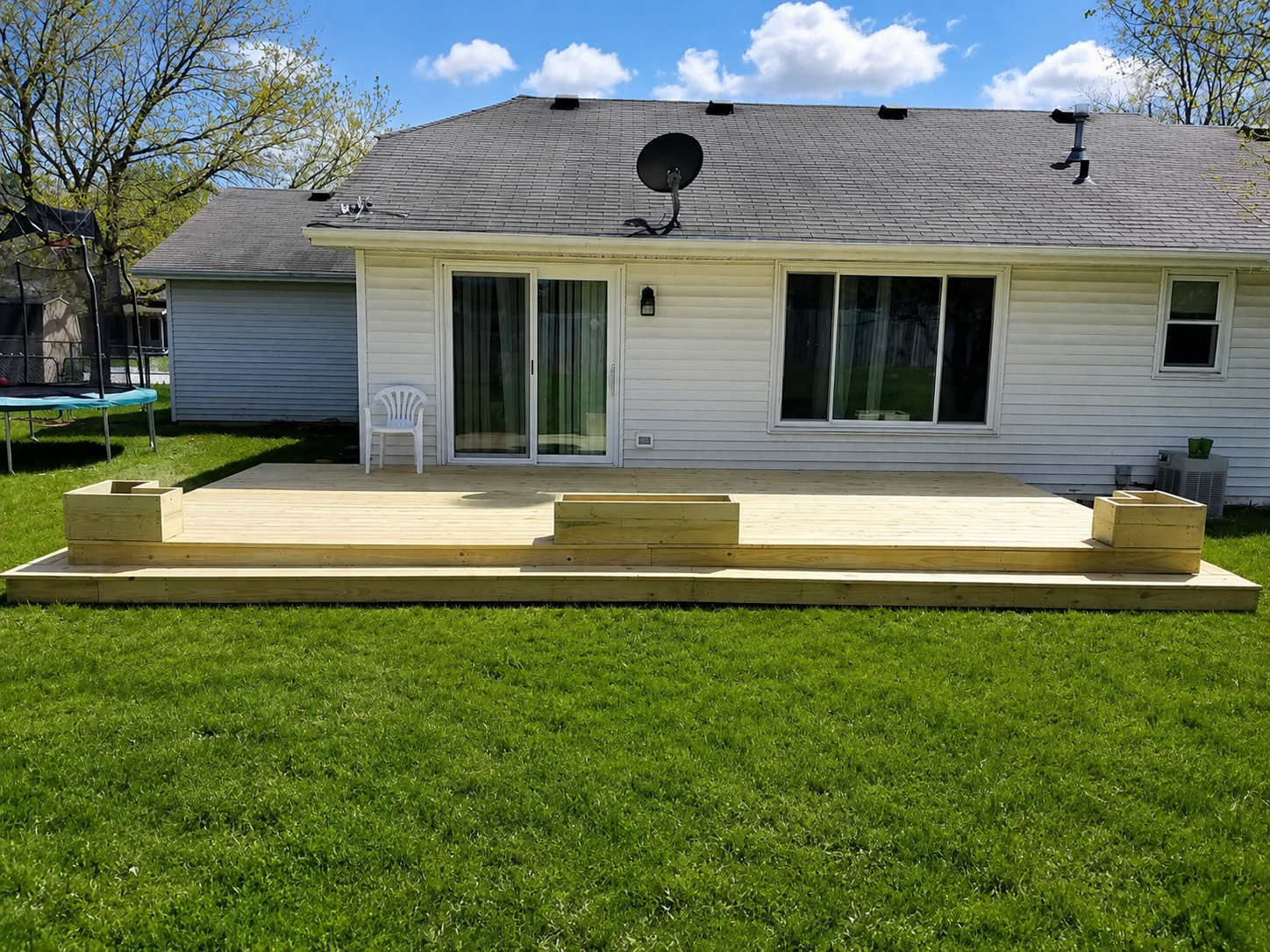 Backyard patio with sliding glass doors, raised wooden deck, and green lawn behind a white house