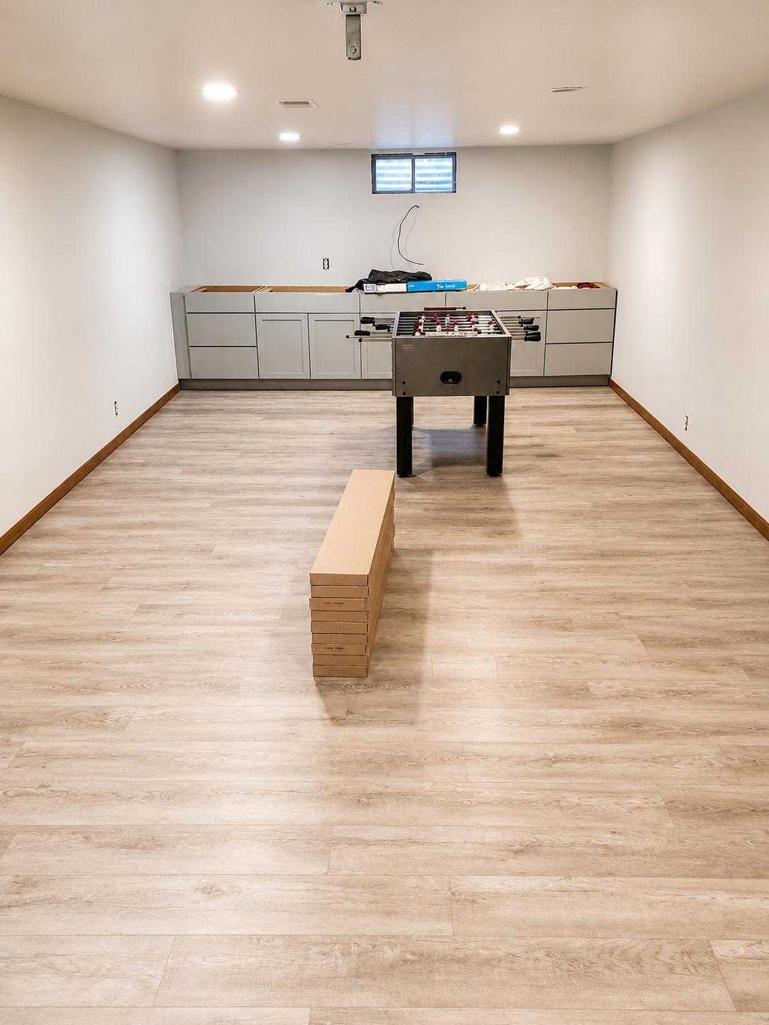 Empty room with light wood floor, white walls, back counter, and a black table with boxes in the center.