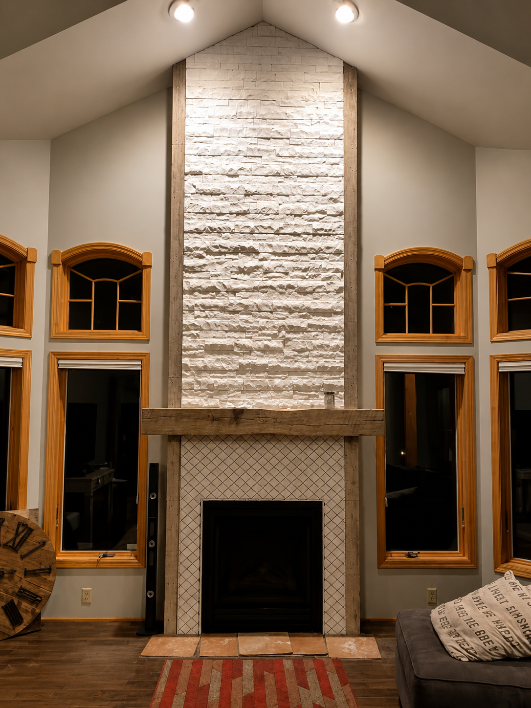 Living room with tall stone fireplace, vaulted ceiling, and wood-trimmed windows