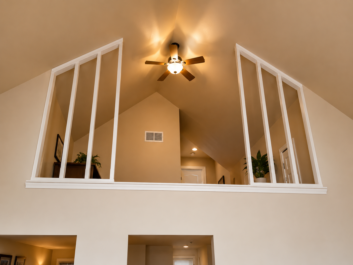 Loft interior with vaulted ceiling, ceiling fan, and white railing overlooking an upper landing.