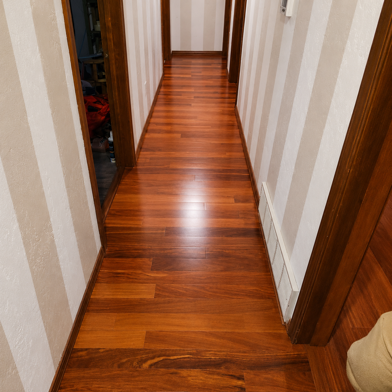 Narrow hallway with glossy wooden floor and striped wallpaper, viewed toward a doorway at the end
