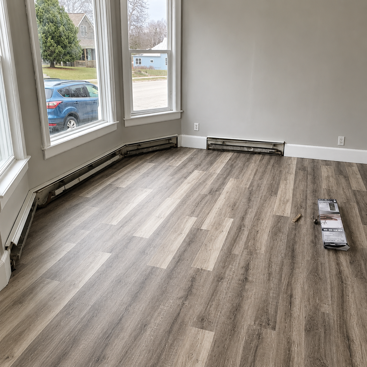 Empty room with gray walls, large bay windows, and wood-look flooring being installed