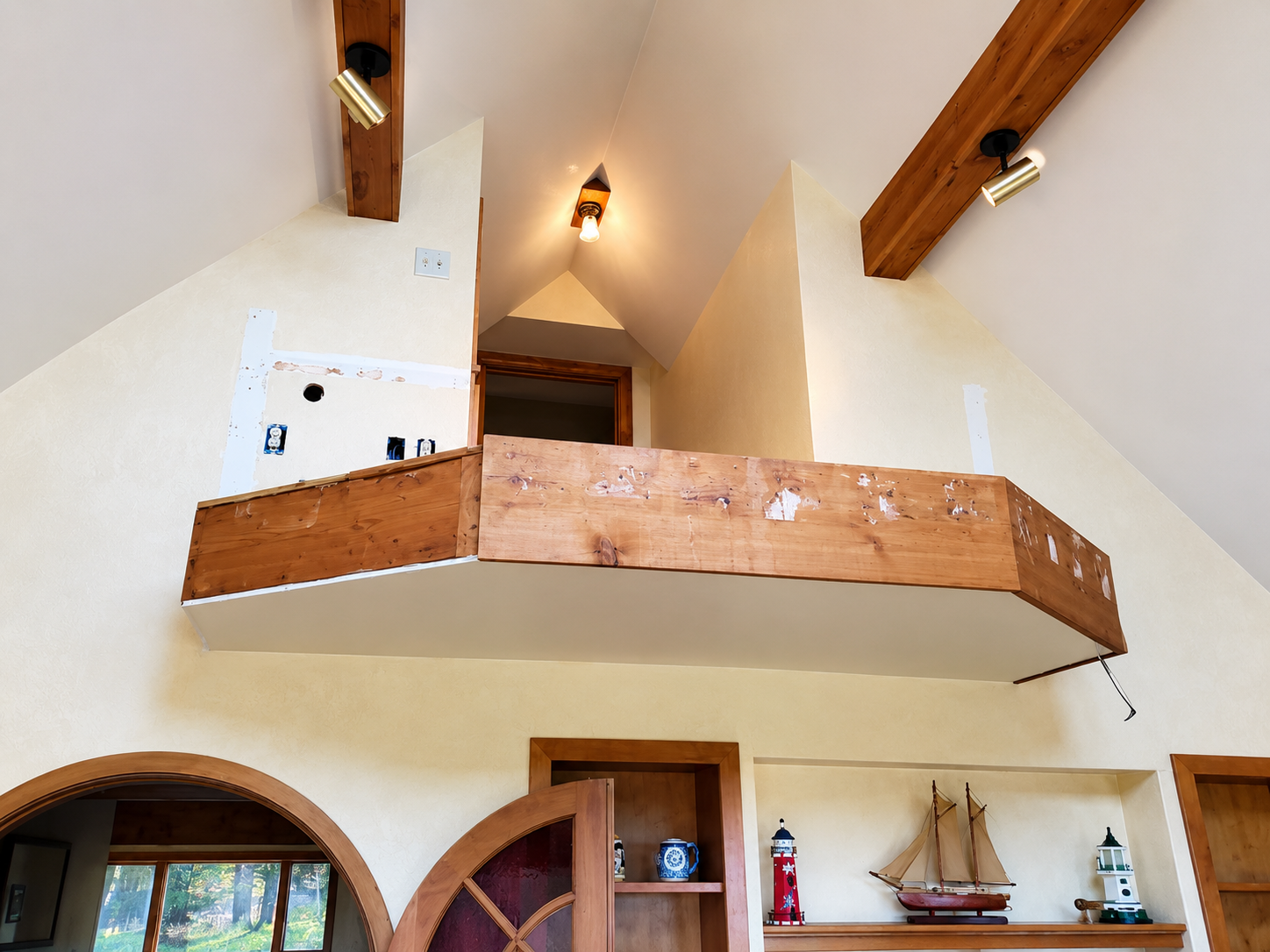 Loft interior with wooden balcony, vaulted ceiling, wall sconce, and arched shelves below