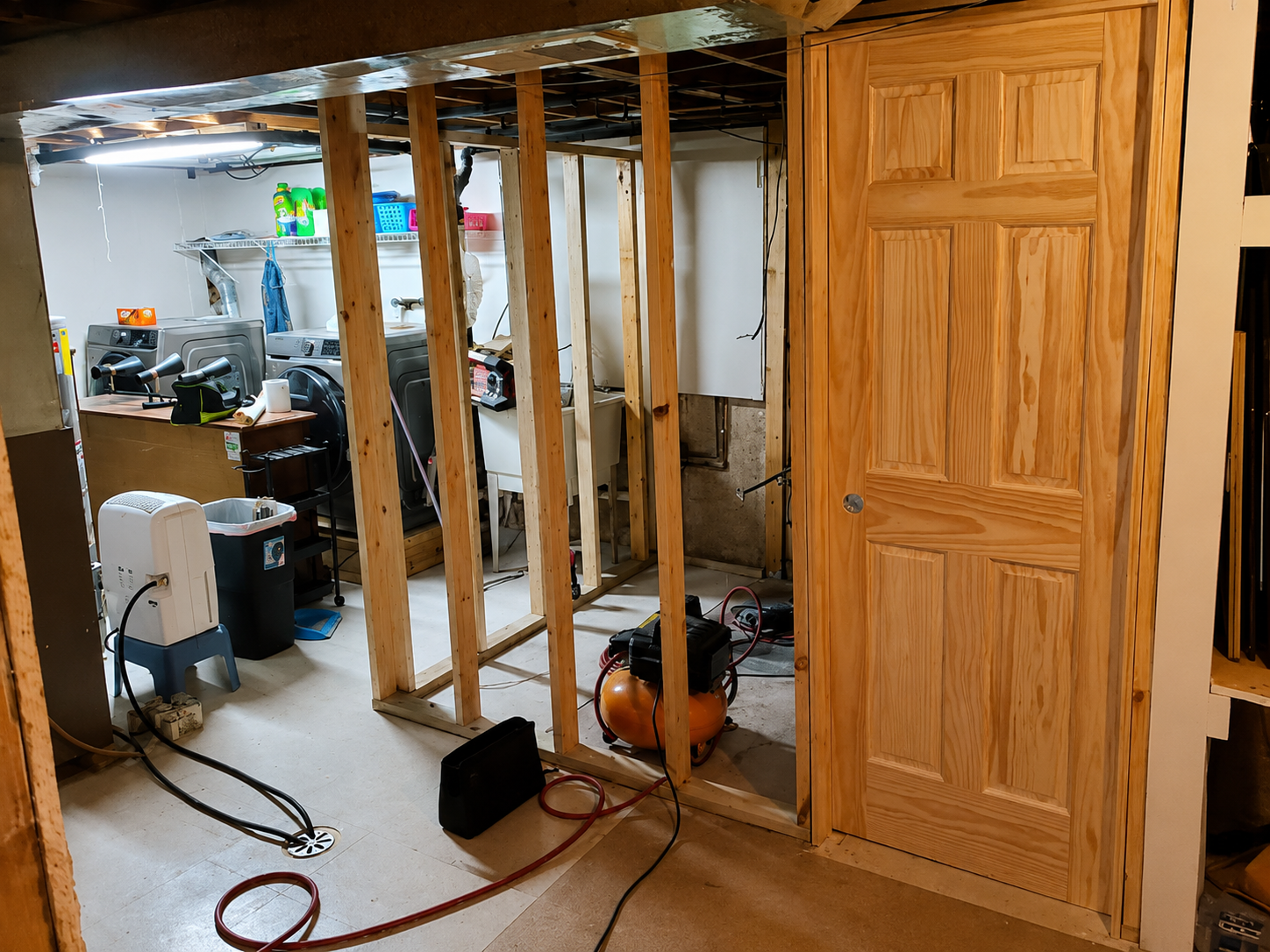 Partially finished basement with exposed wooden studs, tools, and a closed wooden door