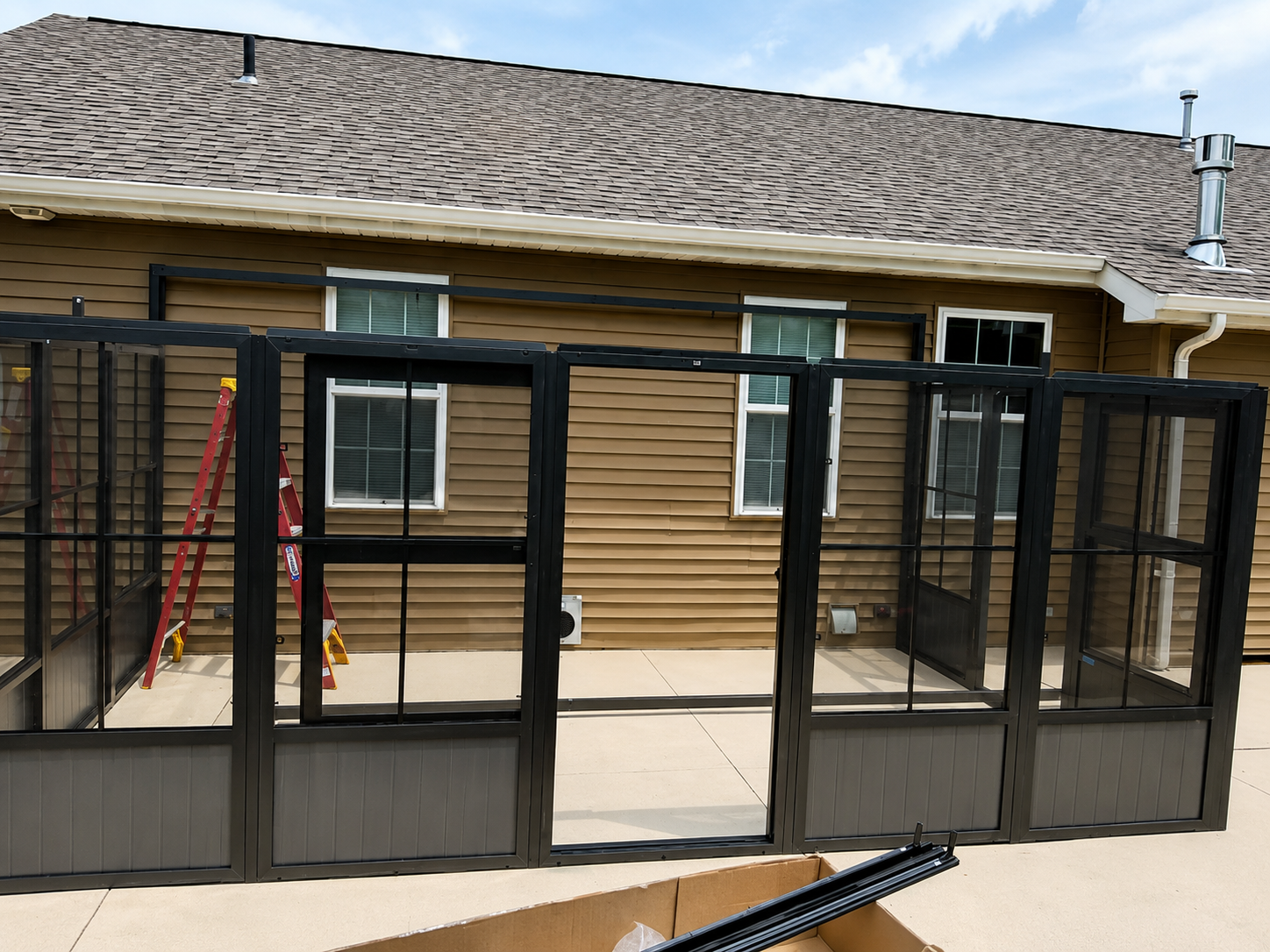 Black metal pet enclosure on a concrete patio beside a tan house with a shingled roof