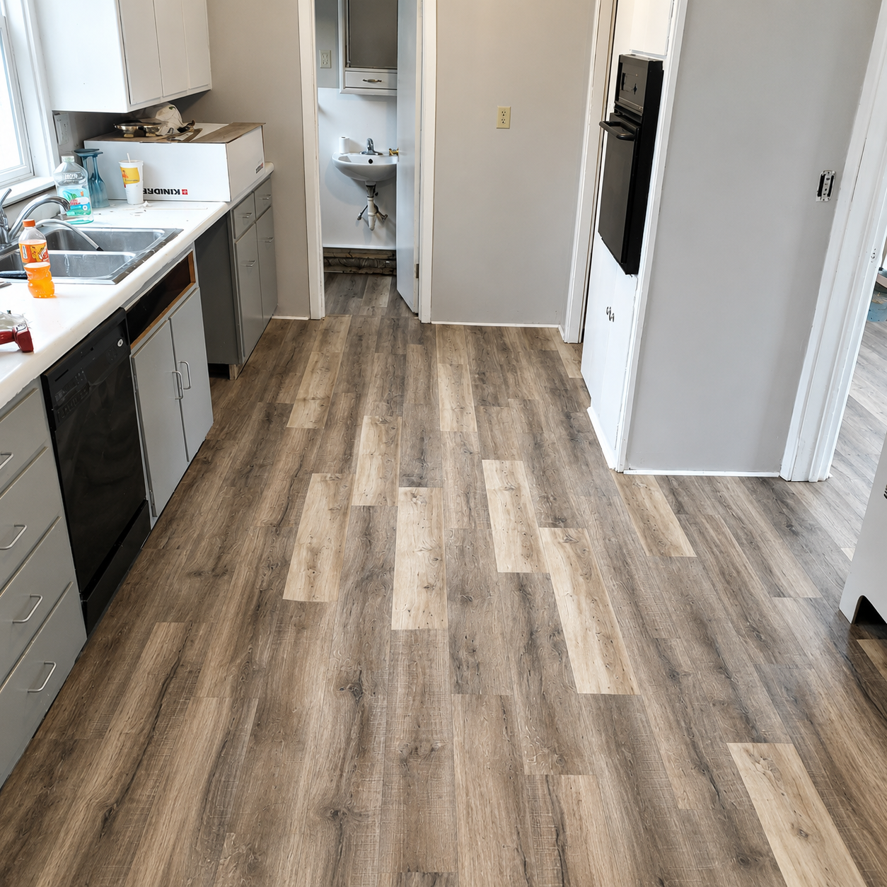 Empty kitchen hallway with wood-look flooring, white cabinets, sink, and open pantry doors.