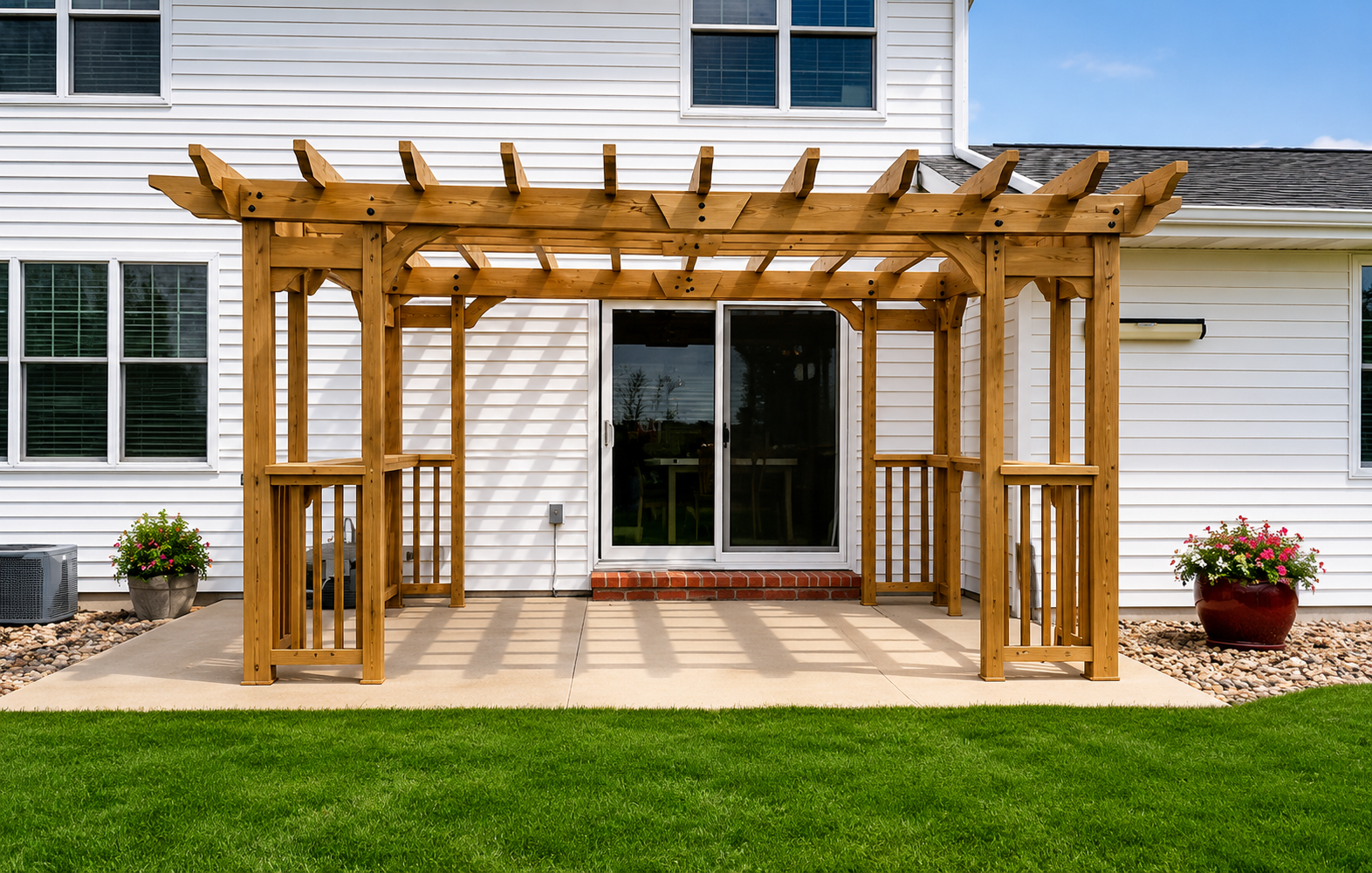 Wooden pergola over a patio outside a white house with sliding glass doors and potted plants
