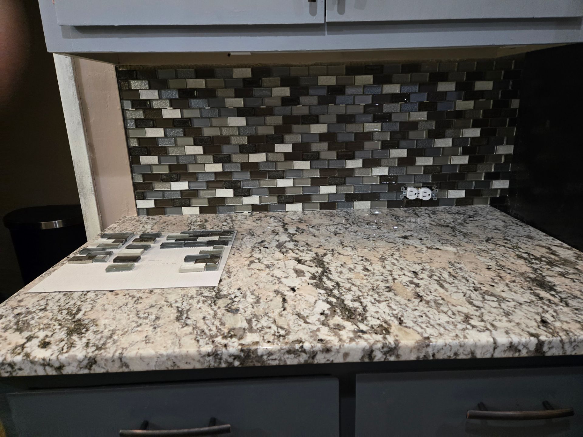 Kitchen countertop with granite surface, mosaic tile backsplash, stovetop, and cabinets underneath