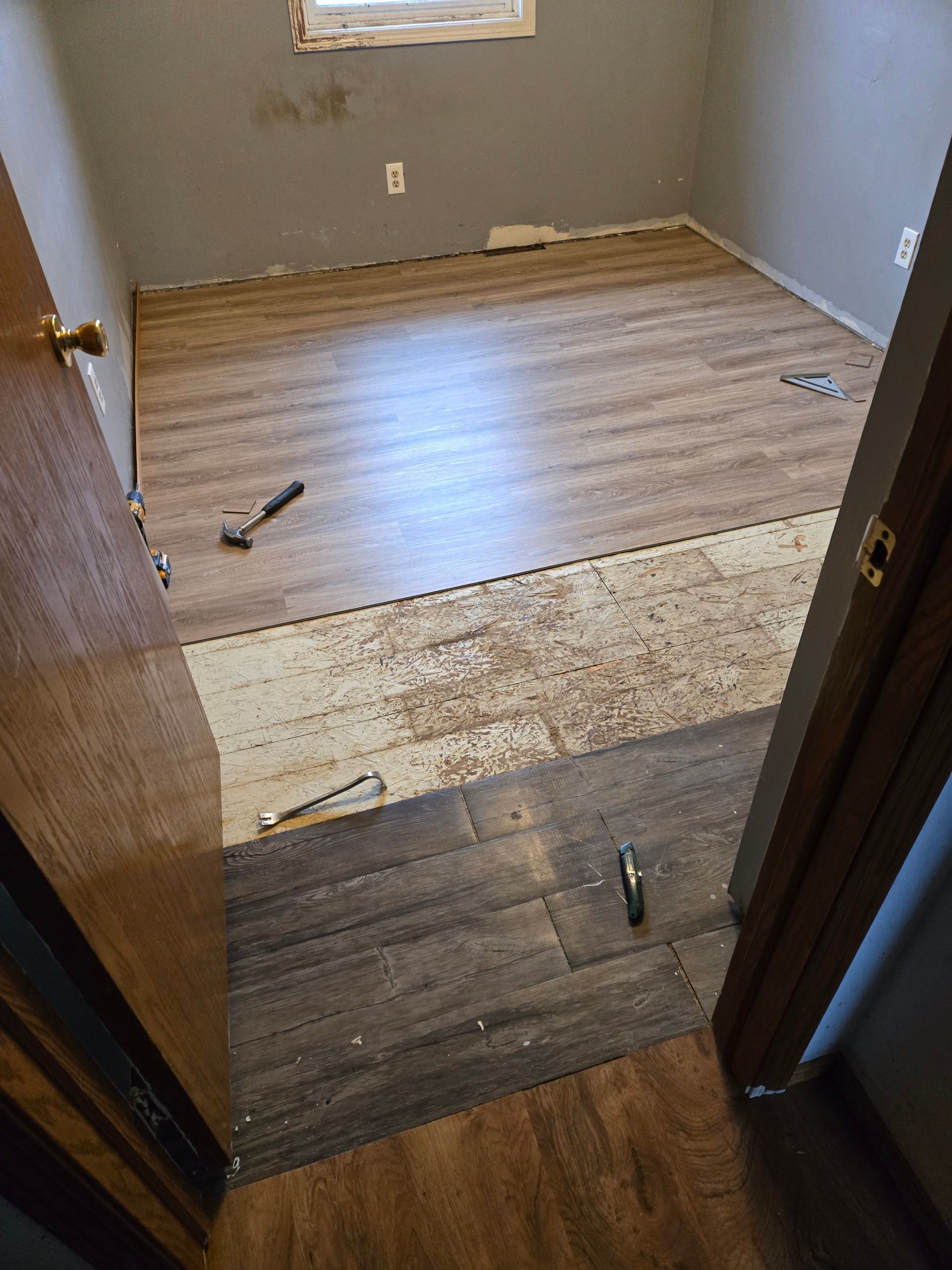 Partially stripped room with exposed subfloor and tools on the floor during renovation