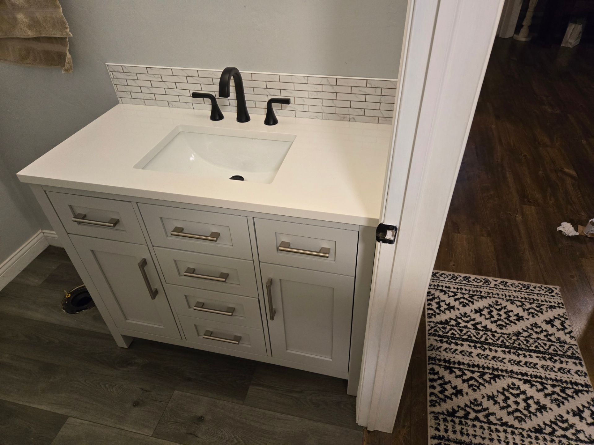 White bathroom vanity with sink and black faucet beside a doorway, with a patterned rug on the floor