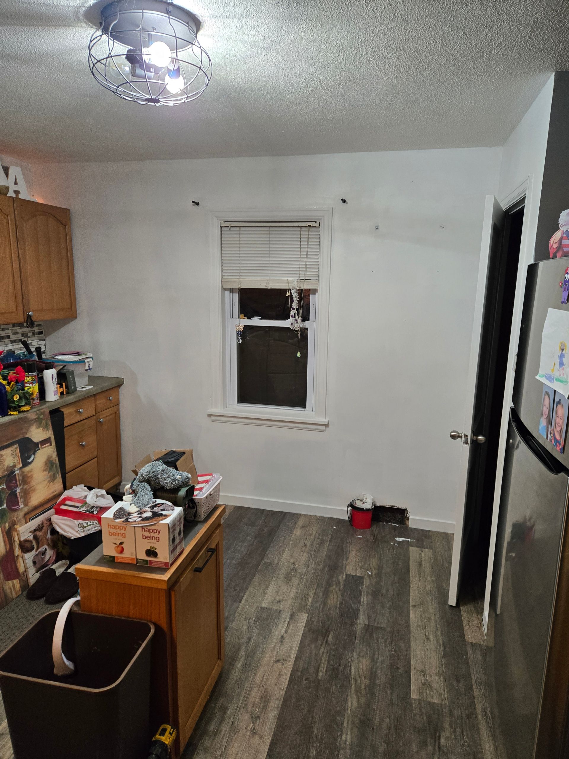 Small kitchen with cabinets, countertop clutter, a window, gray wood floor, and a ceiling light.