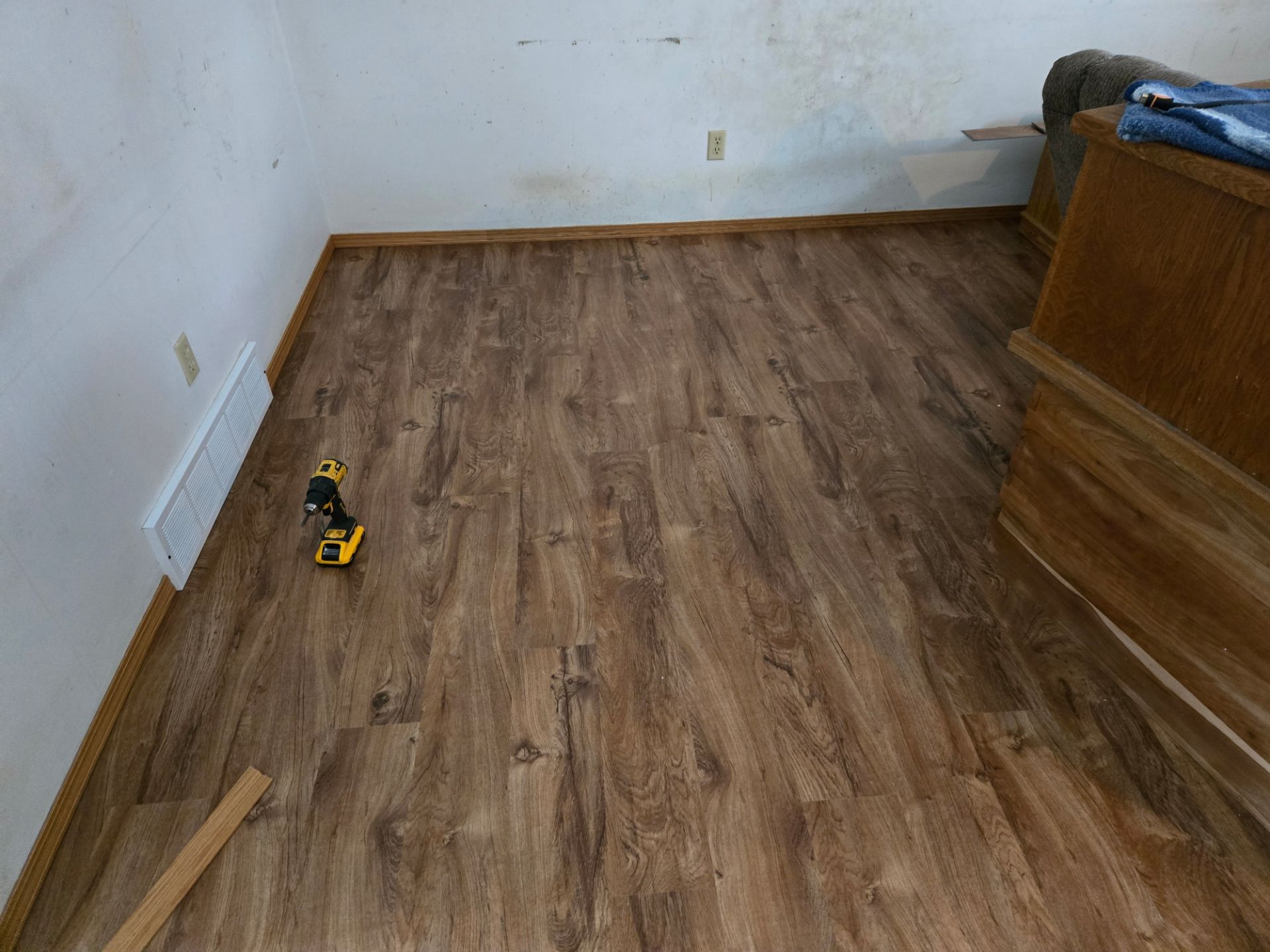 Empty room with wood-look flooring being installed, with tools and trim along the walls.