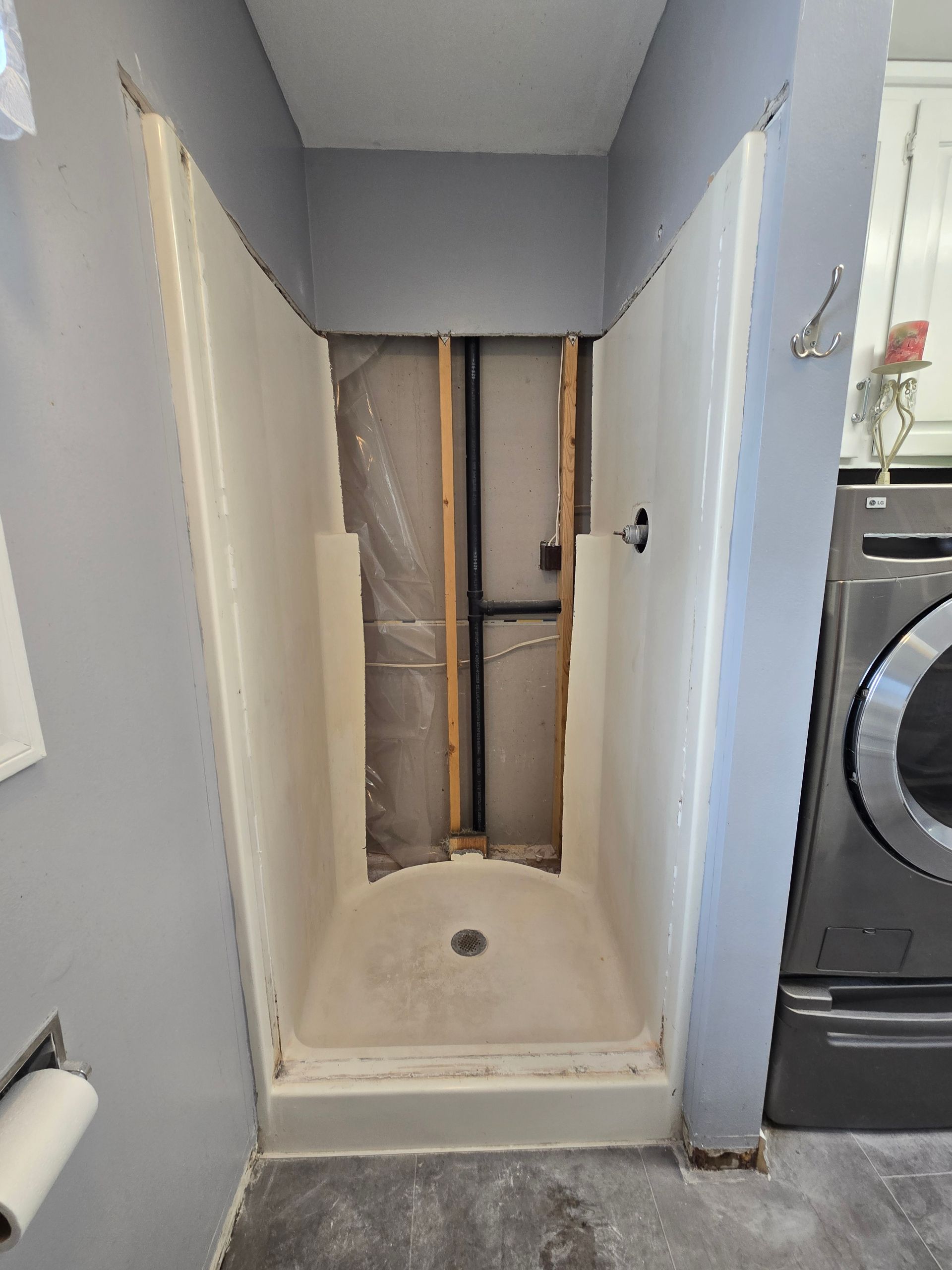 Small shower alcove under renovation with exposed wall framing and a white shower base.