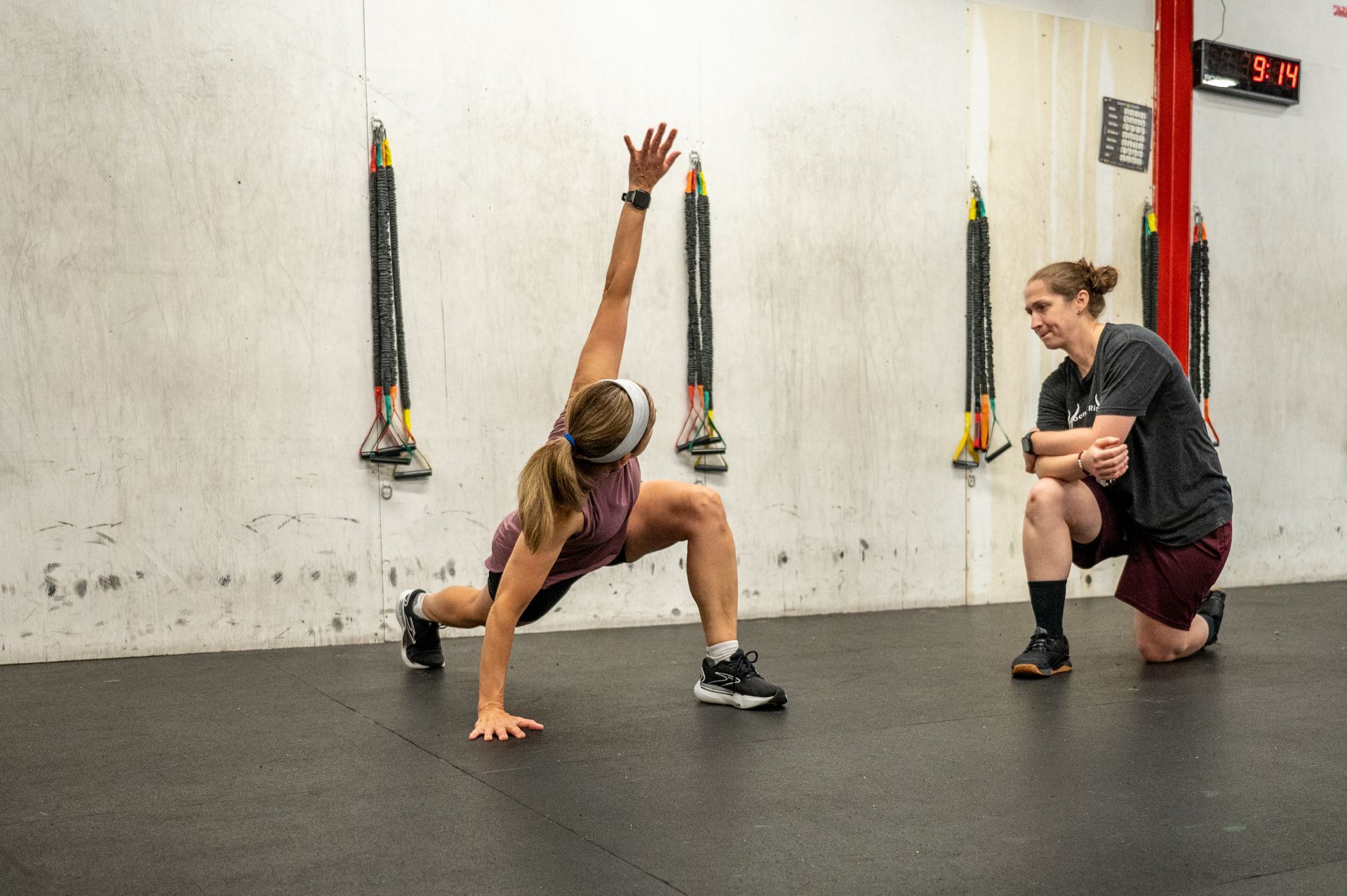 A woman is doing a plank exercise in a gym while a man watches.