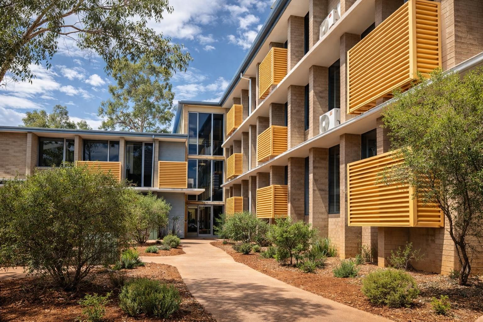 A white building with wooden privacy screens under a corrugated metal awning, surrounded by green shrubs.