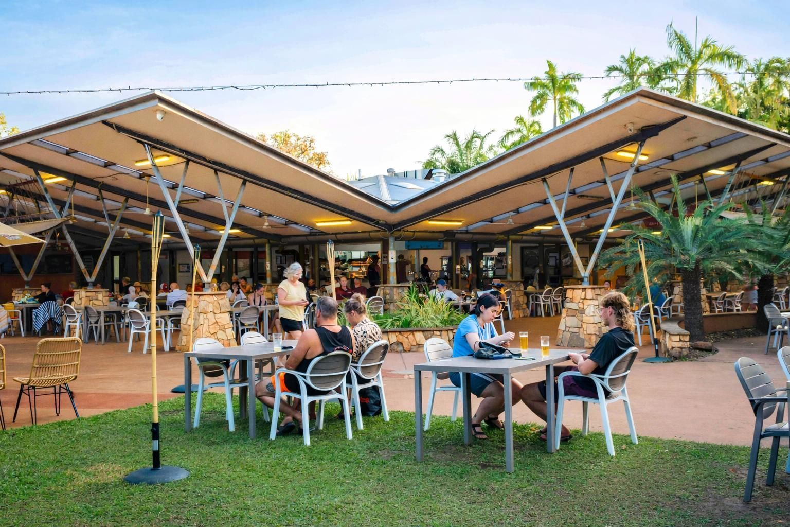 A white building with wooden privacy screens under a corrugated metal awning, surrounded by green shrubs.