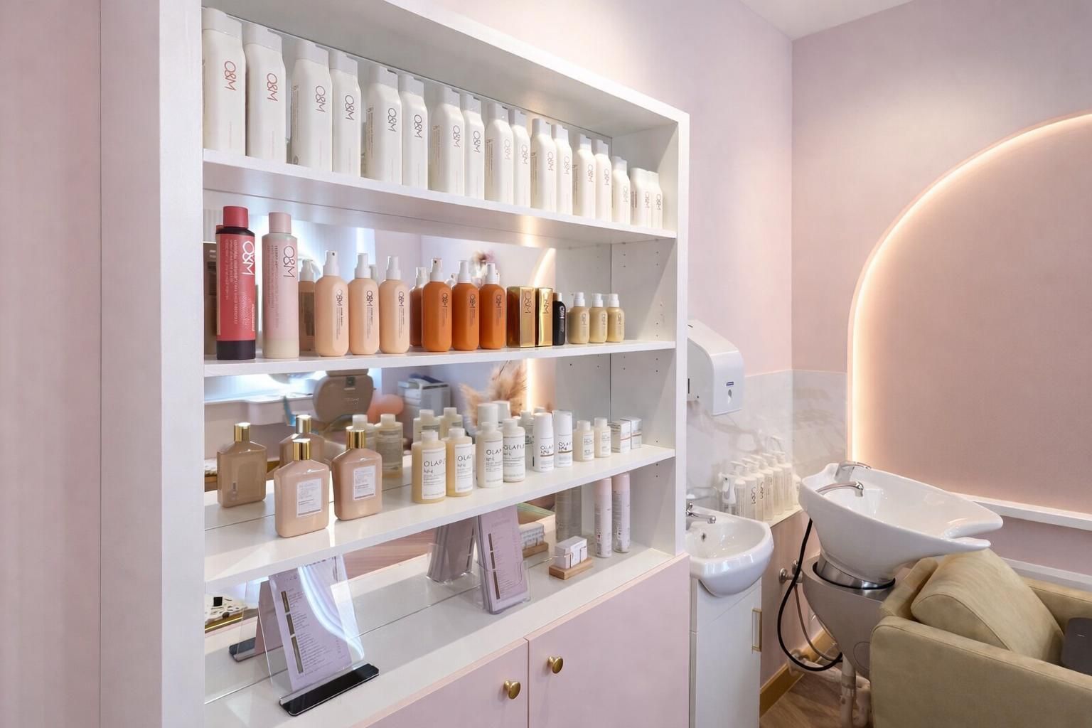 A salon display shelf filled with rows of hair care bottles, next to a hair washing station with a sink and chair.
