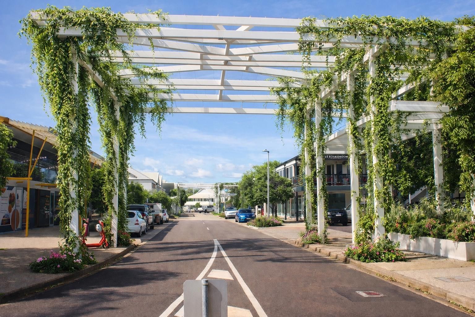 A street framed by a white wooden pergola covered in green vines, with buildings and parked cars on either side.