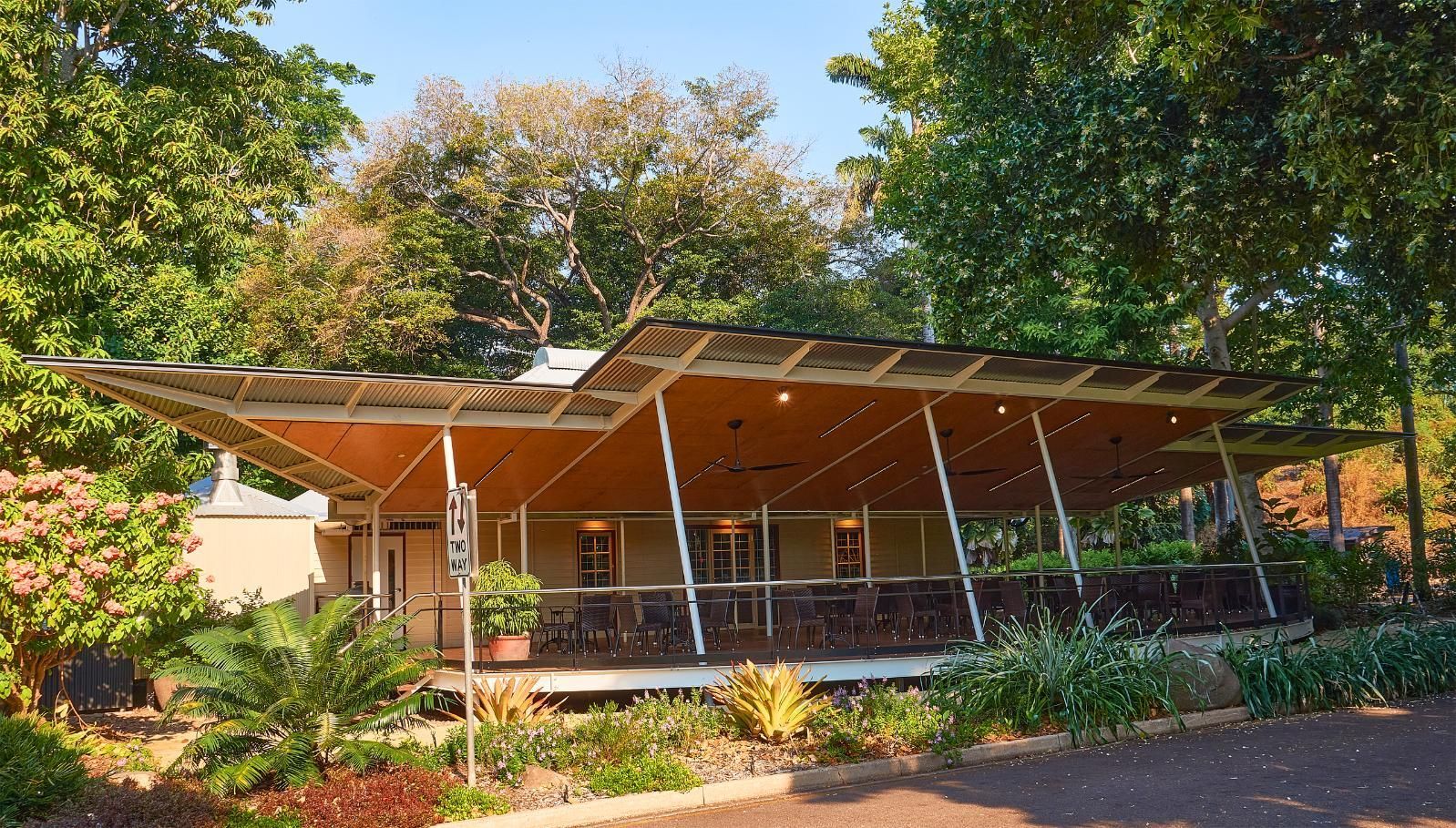 A modern building with a sweeping, angular wooden roof and outdoor seating, nestled in a lush, tree-filled park setting.