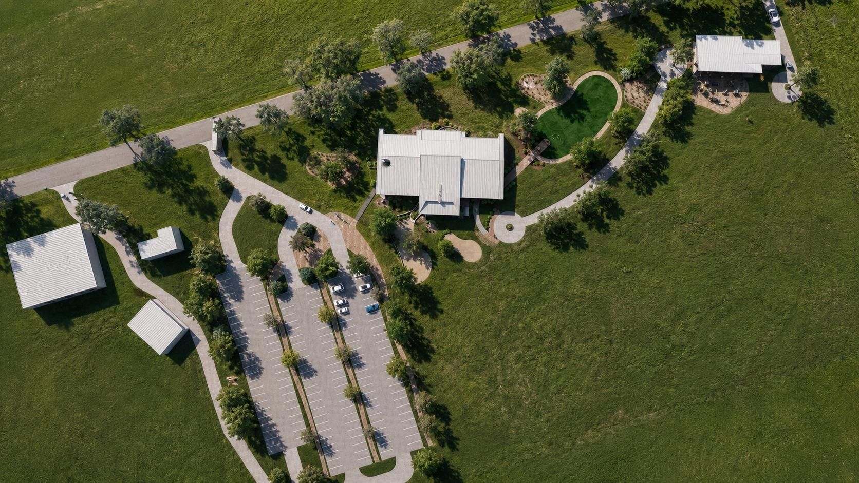 An aerial view of a rural facility with a white main building, parking lot, landscaped gardens, and surrounding fields.