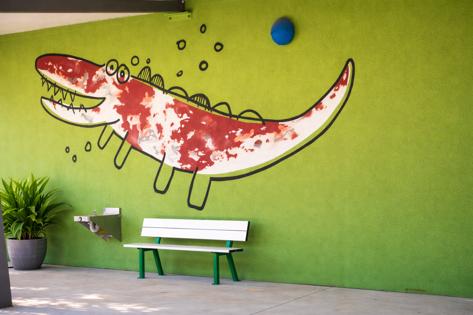 A green wall features a mural of a stylized red alligator, a white bench, and a drinking fountain.