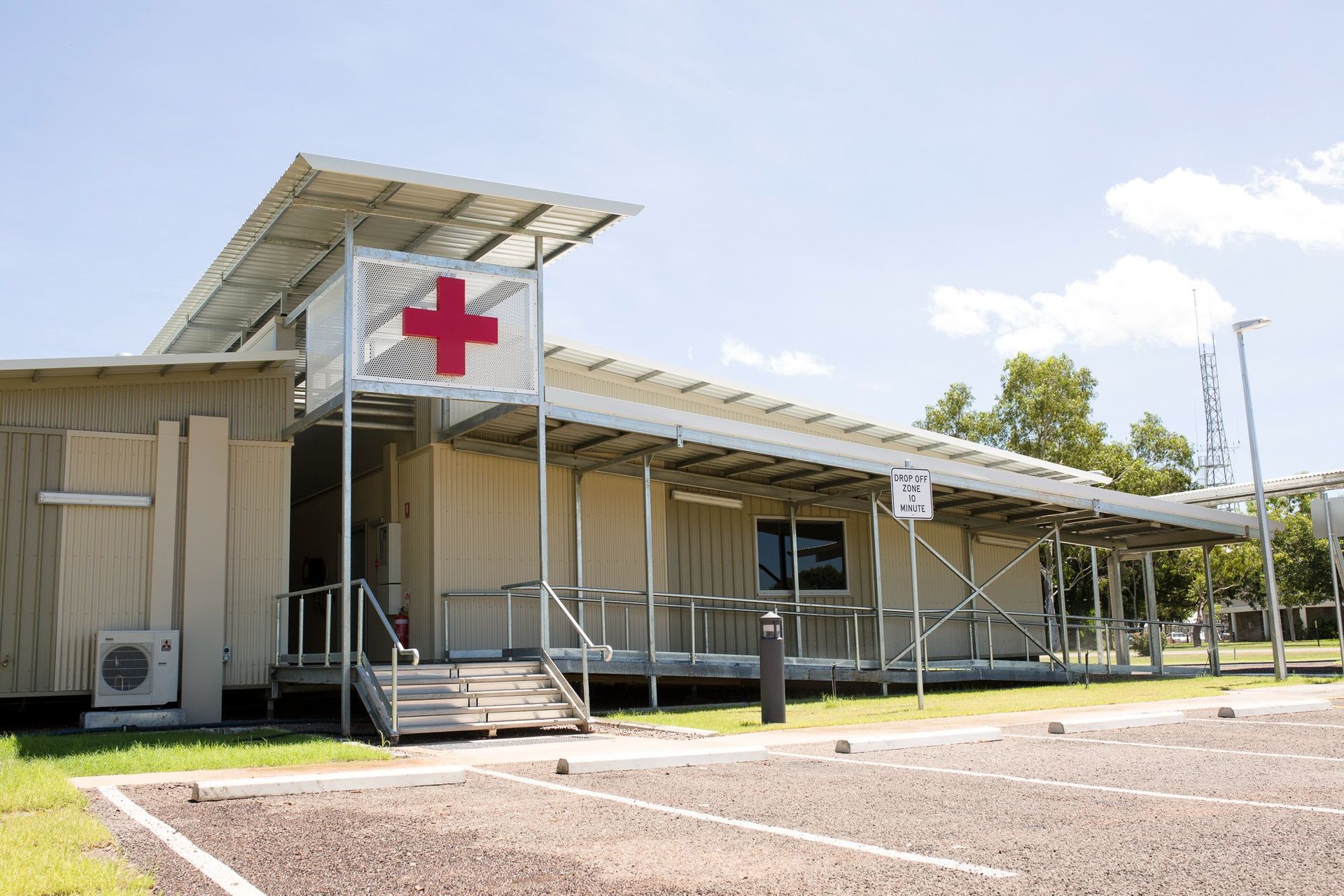 A white building with wooden privacy screens under a corrugated metal awning, surrounded by green shrubs.