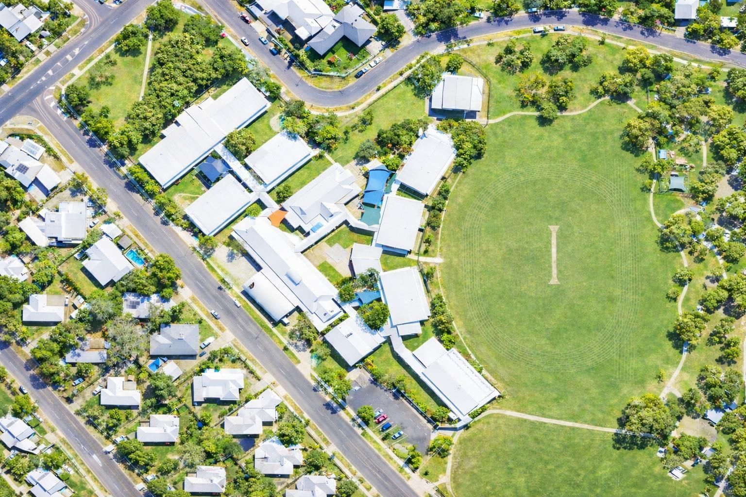 Aerial view of a school campus with white roof buildings and a large, green circular sports field.