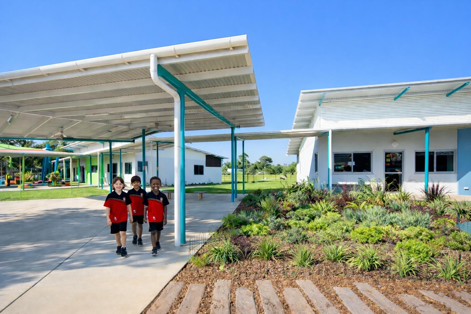 Three students walk on a concrete path outside modern school buildings with large white overhangs and green accents.