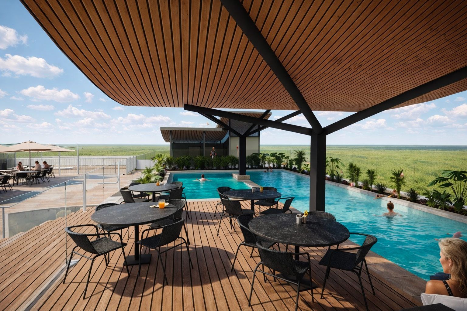 An outdoor pool terrace with dining tables, wooden decking, and a slatted canopy, overlooking a vast, flat grassy landscape.