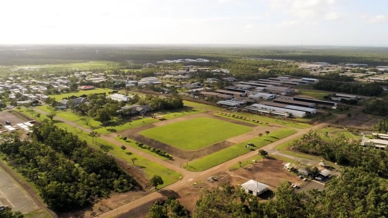 An aerial view of a sprawling residential community featuring a central green field surrounded by trees and houses.