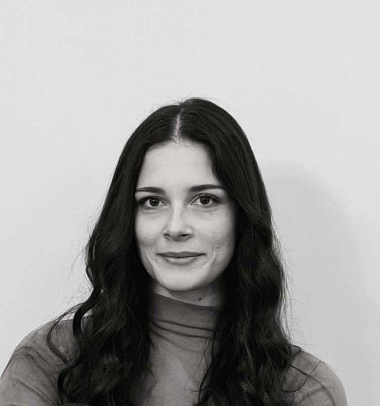 A portrait of a person with long, wavy dark hair, wearing a high-necked top, centered against a plain, light background.