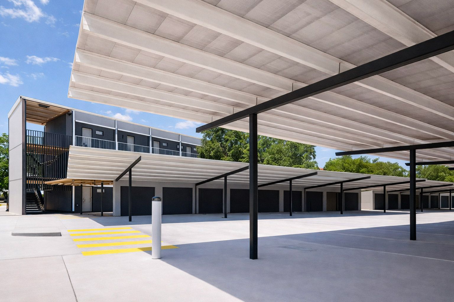 A multi-level apartment building with a white perforated roof structure providing shade over a paved parking area.