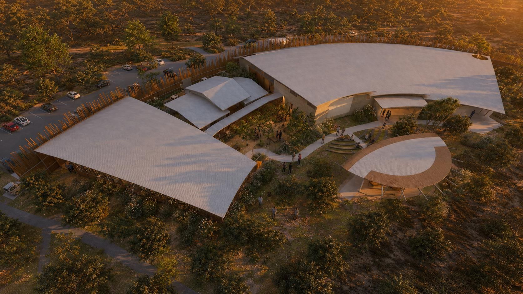 An aerial view of a modern, curved building with tiered, light-colored roofs set within a wooded landscape.