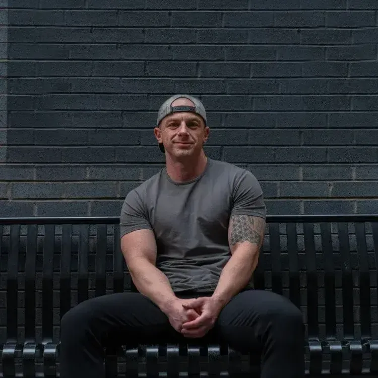 A man is sitting on a bench in front of a brick wall