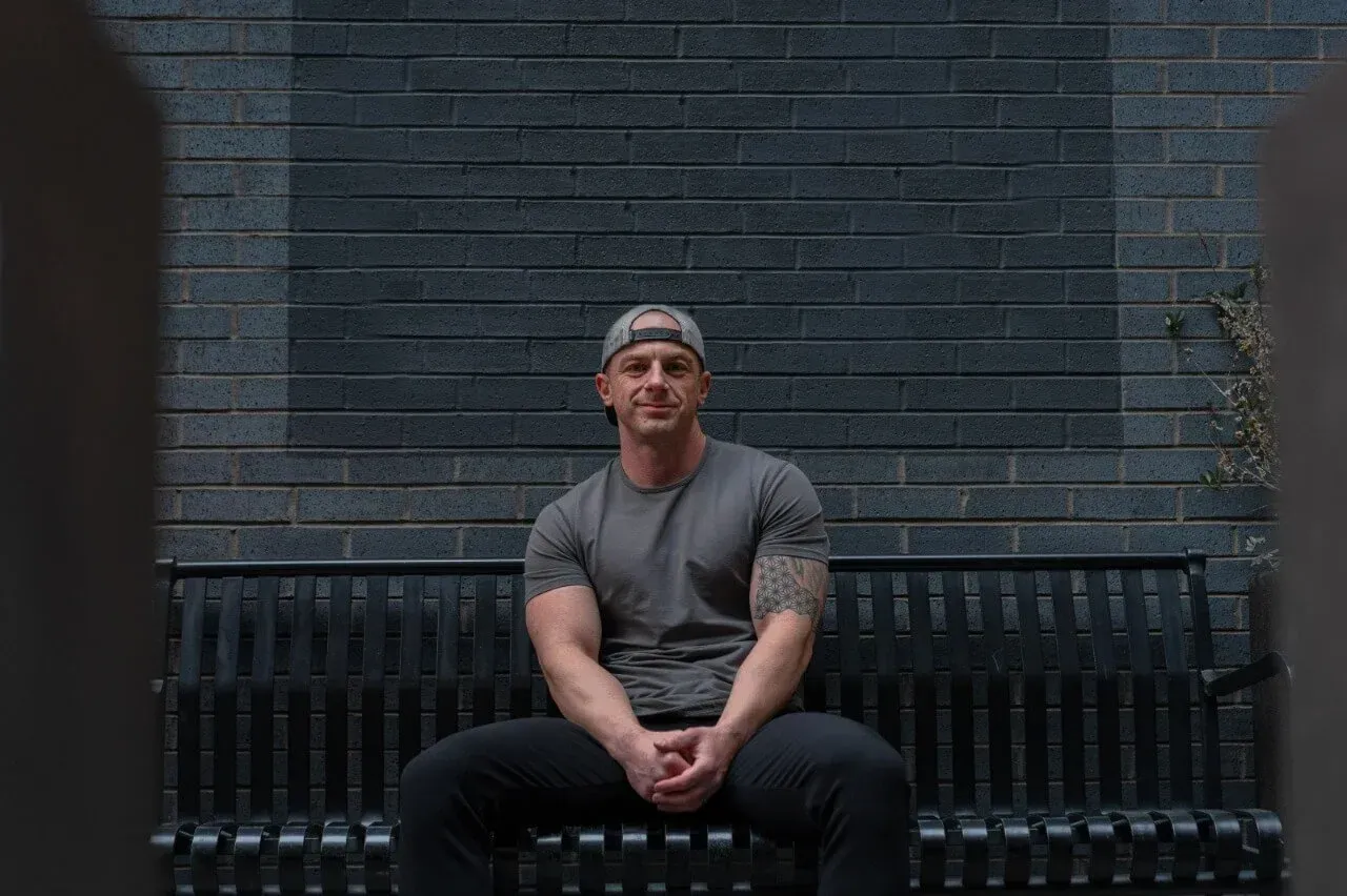 A man is sitting on a bench in front of a brick wall.