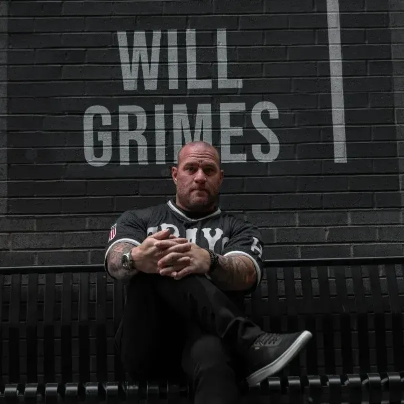 A man is sitting on a bench in front of a brick wall that says will grimes.