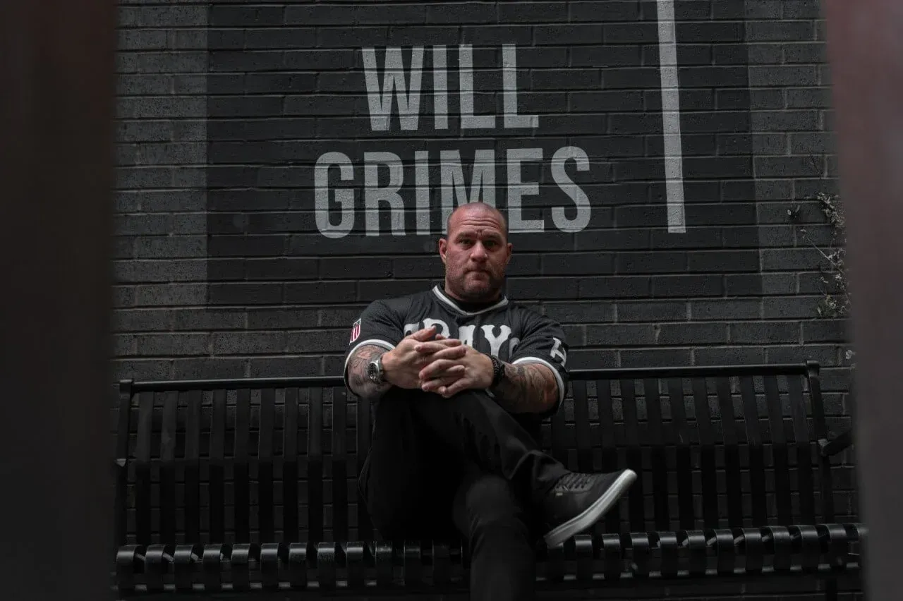 A man is sitting on a bench in front of a brick wall.