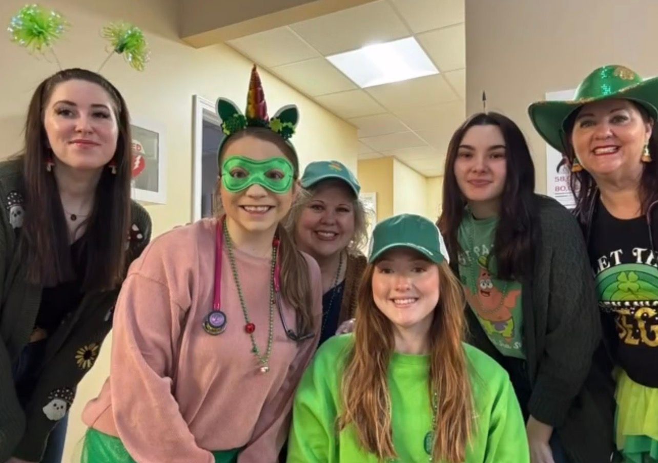 Five women in green and black St. Patrick’s Day outfits posing indoors, smiling at the camera.