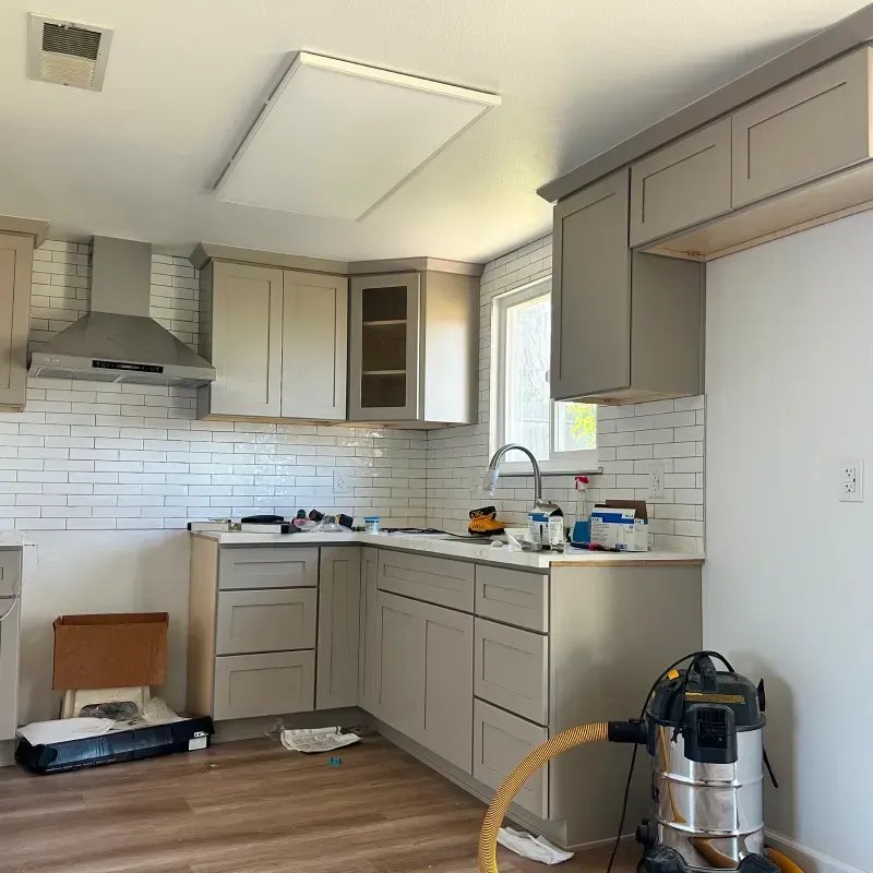 Modern kitchen renovation with gray cabinets, white subway tile, and cleaning supplies on the counter
