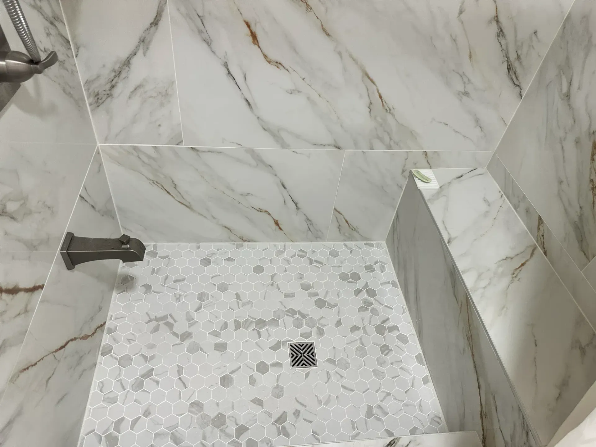 Marble-tiled shower stall with a mosaic floor and wall-mounted fixtures