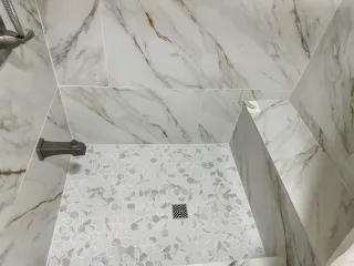 Marble-tiled shower stall with a mosaic floor and wall-mounted fixtures