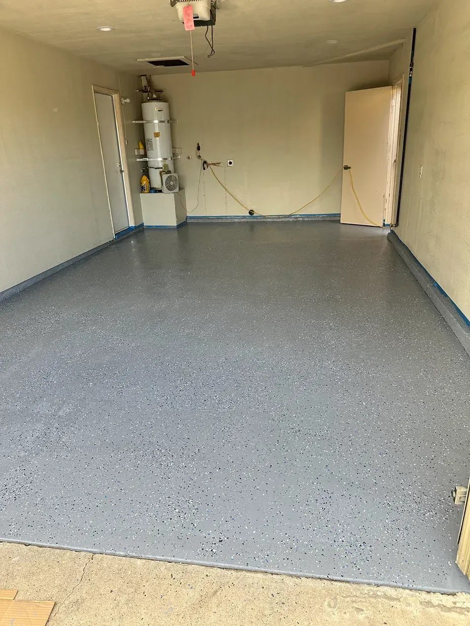 Empty garage interior with gray speckled floor and beige walls, water heater at the back left.