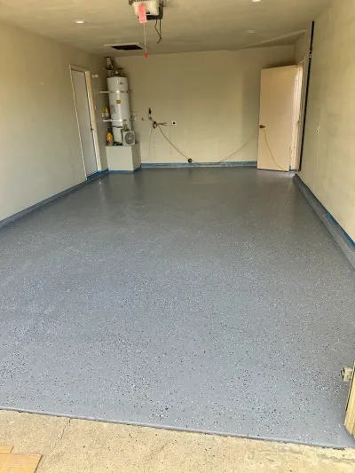 Empty garage interior with gray speckled floor and beige walls, water heater at the back left.