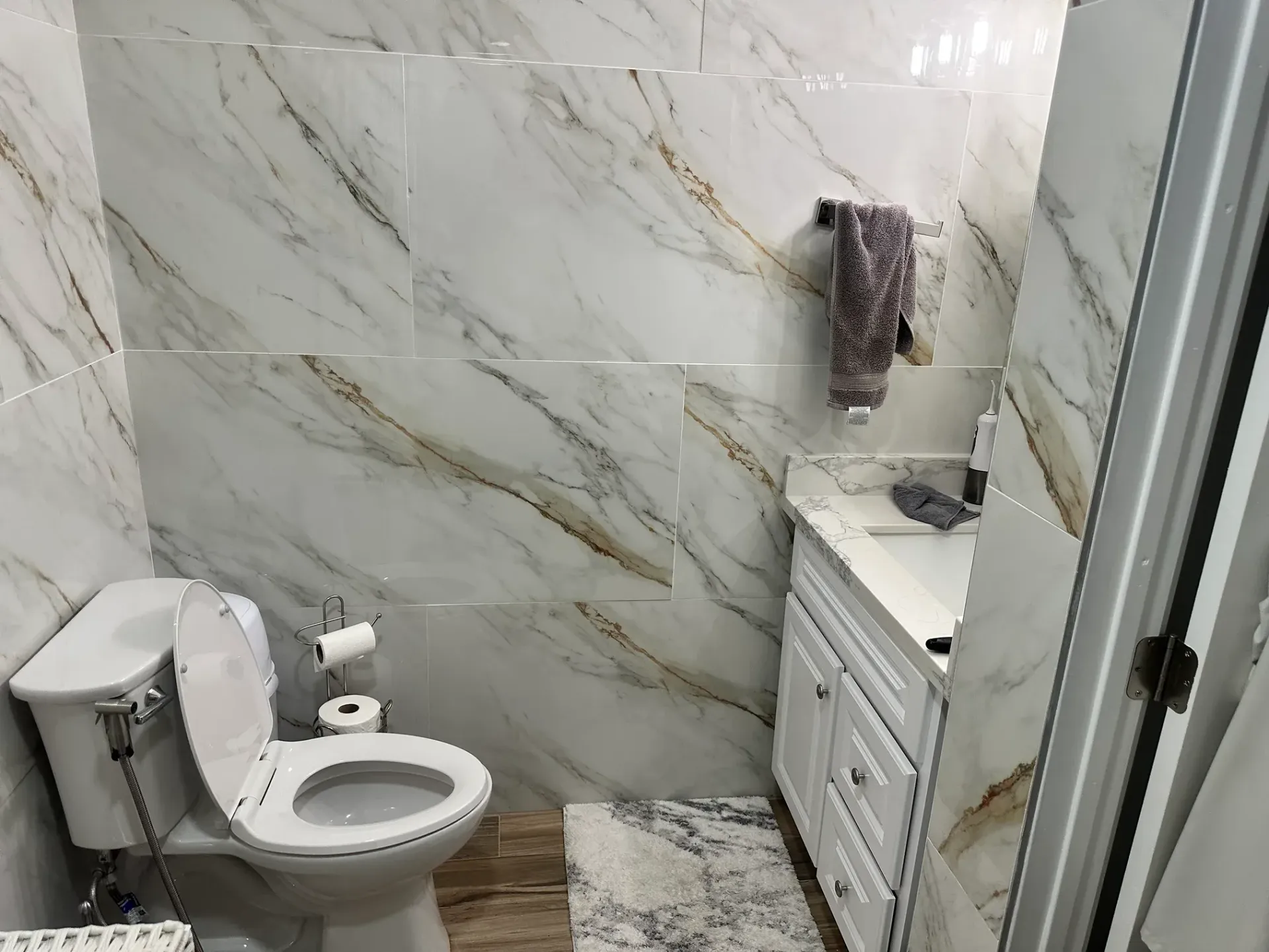 Small bathroom with toilet, vanity, marble-look tile walls, and glass shower door