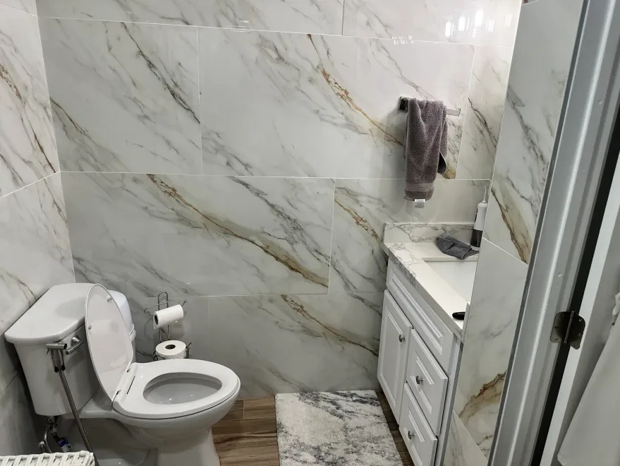 Small bathroom with toilet, vanity, marble-look tile walls, and glass shower door