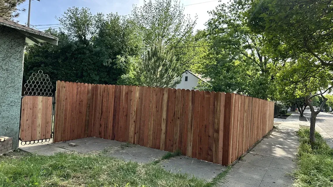 Wooden fence enclosing a concrete patio beside a house, with trees and grass in the yard.