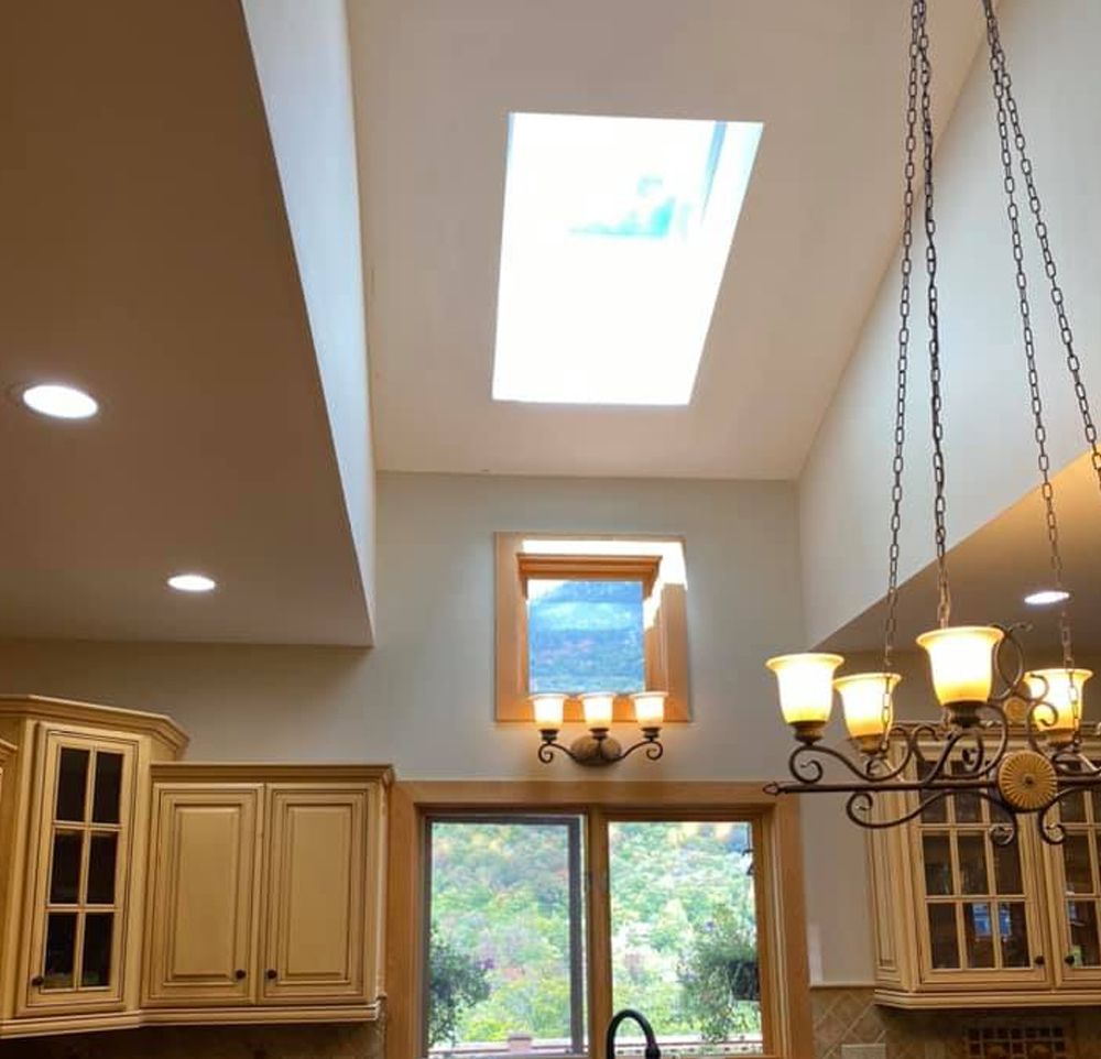 Bright kitchen with skylight, chandelier, cream cabinets, and a window over the sink